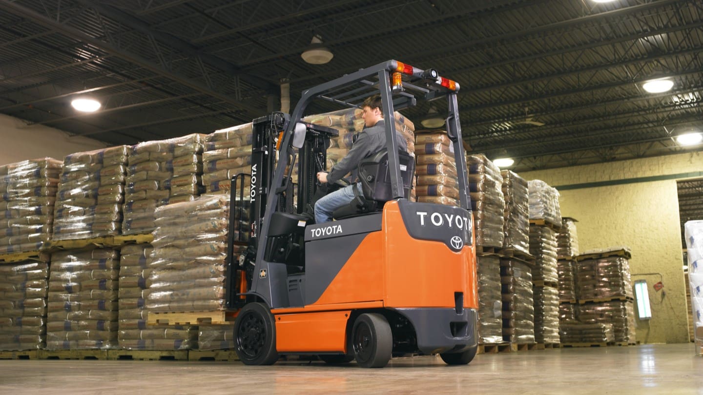 A worker operates a high-spec Toyota forklift inside a warehouse, skillfully maneuvering through aisles stacked with large, wrapped pallets. This image showcases the efficiency and reliability of forklift hire services in Surrey, demonstrating how such equipment is essential for smooth operational logistics in various industrial settings.